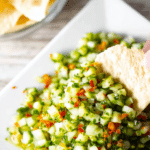 A colorful bowl of dill pickle salsa with fresh herbs and tortilla chips for dipping.