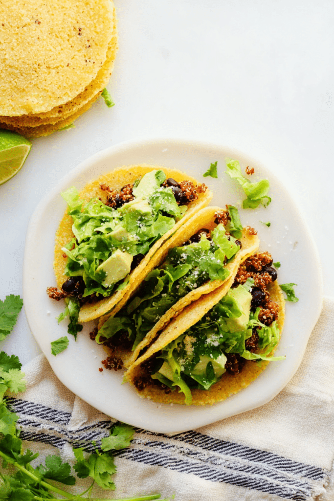 Delicious quinoa black bean tacos with avocado sauce, cilantro, and lime on a rustic wooden table.