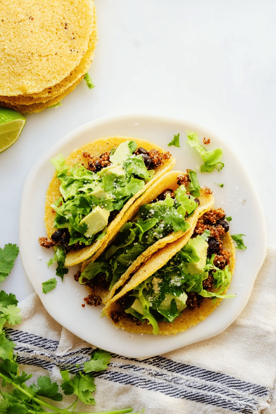 Delicious quinoa black bean tacos with avocado sauce, cilantro, and lime on a rustic wooden table.
