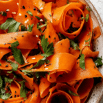 Raw carrot salad with parsley and sesame seeds in a bowl on a wooden table.