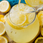 Glass of homemade lemonade garnished with lemon slice and mint on a wooden table.