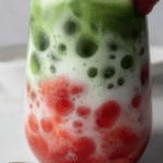 Close-up of a refreshing strawberry matcha latte with layered strawberry purée and matcha, garnished with fresh strawberries.
