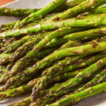 Close-up of roasted asparagus garnished with lemon zest on a wooden table.