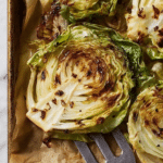 Roasted cabbage steak with seasoning and lemon wedges on a wooden table
