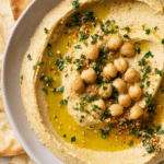 Delicious roasted garlic hummus with olive oil, parsley, and chickpeas, served with pita bread.