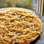 Slice of leftover pasta frittata garnished with herbs on a wooden table.