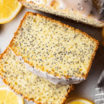 Sliced lemon poppy seed loaf on a wooden table with fresh lemons and poppy seeds in the background.