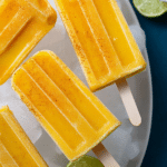 Colorful spicy mango popsicles surrounded by fresh mangoes and spices, ideal for summer treats.