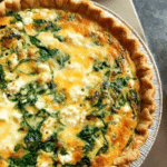Delicious spinach feta quiche on a wooden table, garnished with fresh spinach and feta cheese.