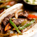 Delicious steak fajitas with colorful peppers and onions served with tortillas.