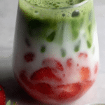 Strawberry matcha latte in a clear glass layered with puréed strawberries and matcha, topped with fresh strawberries.