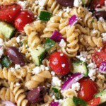 Vibrant Greek pasta salad with rotini, cucumbers, tomatoes, olives, and feta cheese in a glass bowl