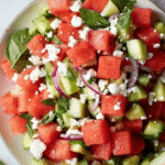 Watermelon salad with feta cheese, cucumber, and fresh mint on a wooden table.