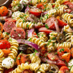 Bowl of zesty Italian pasta salad with cherry tomatoes, bell peppers, and olives, garnished with parsley and Parmesan.