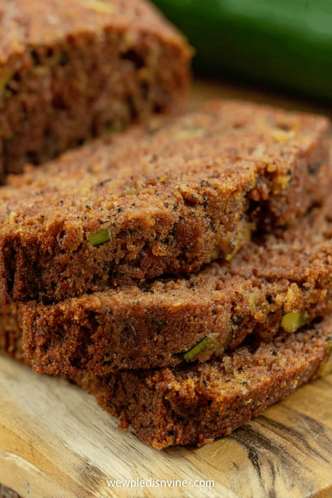 Delicious zucchini bread slice topped with cinnamon, surrounded by fresh zucchini and walnuts.