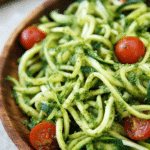 A delicious serving of zucchini noodles with pesto, garnished with cherry tomatoes and Parmesan cheese.