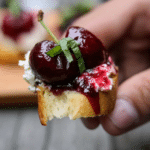 Close-up of balsamic cherry and goat cheese crostini on a rustic wooden board, garnished with fresh basil.