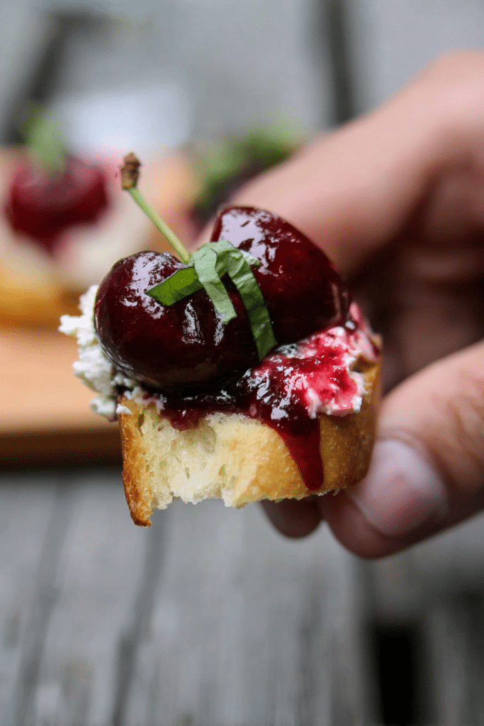 Close-up of balsamic cherry and goat cheese crostini on a rustic wooden board, garnished with fresh basil.