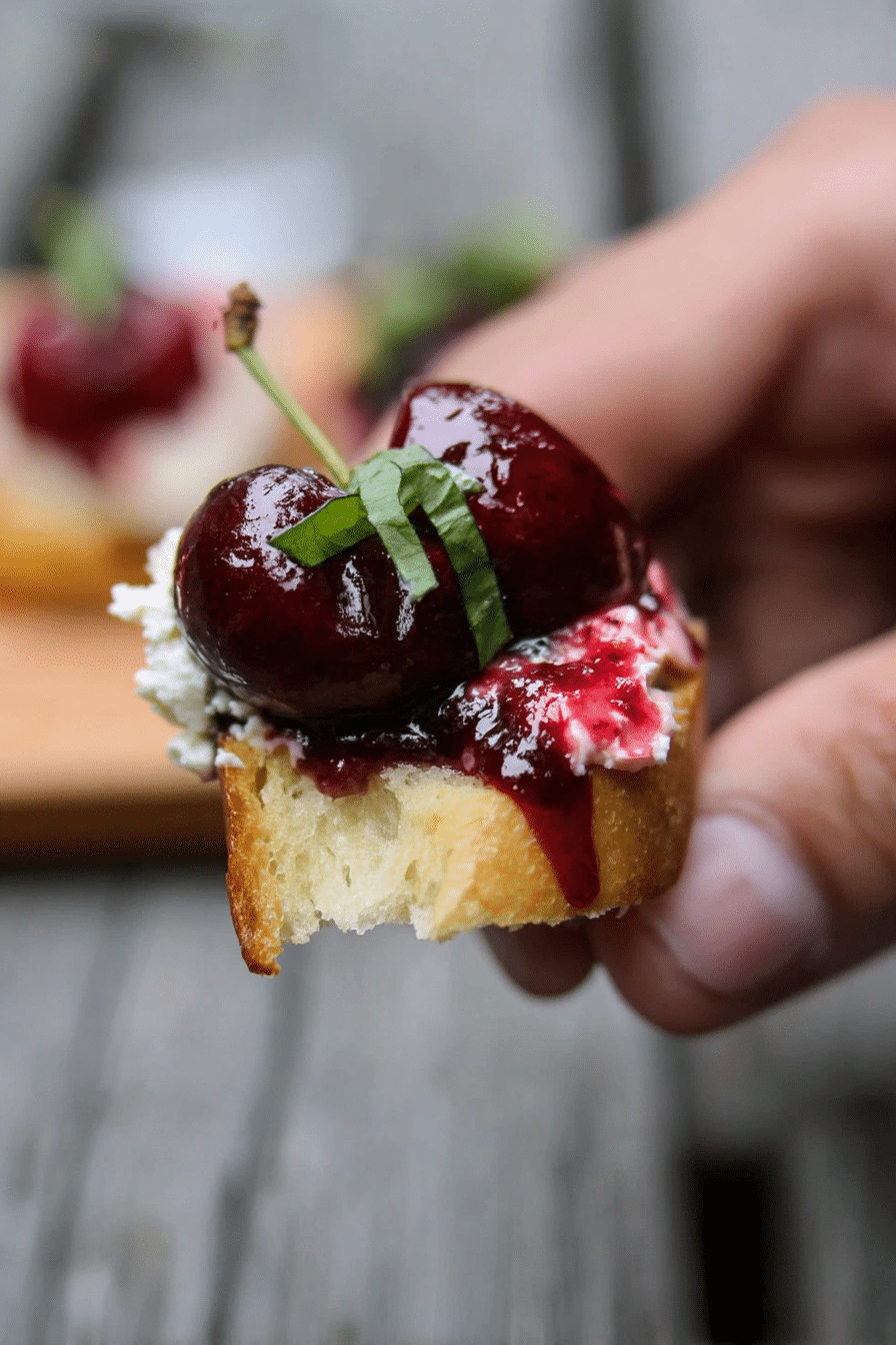 Close-up of balsamic cherry and goat cheese crostini on a rustic wooden board, garnished with fresh basil.