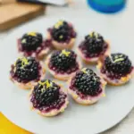 Close-up of beautifully arranged blackberry tarts with fresh blackberries and lemon zest on a wooden serving board.
