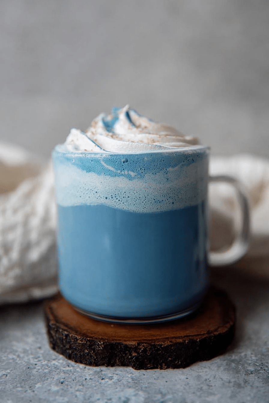 Blue latte with spirulina, topped with dairy-free whipped cream and cinnamon, served in a stylish mug on a rustic wooden table.