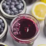 Jars of homemade blueberry lemon jam with fresh blueberries and lemon slices on a rustic wooden background.