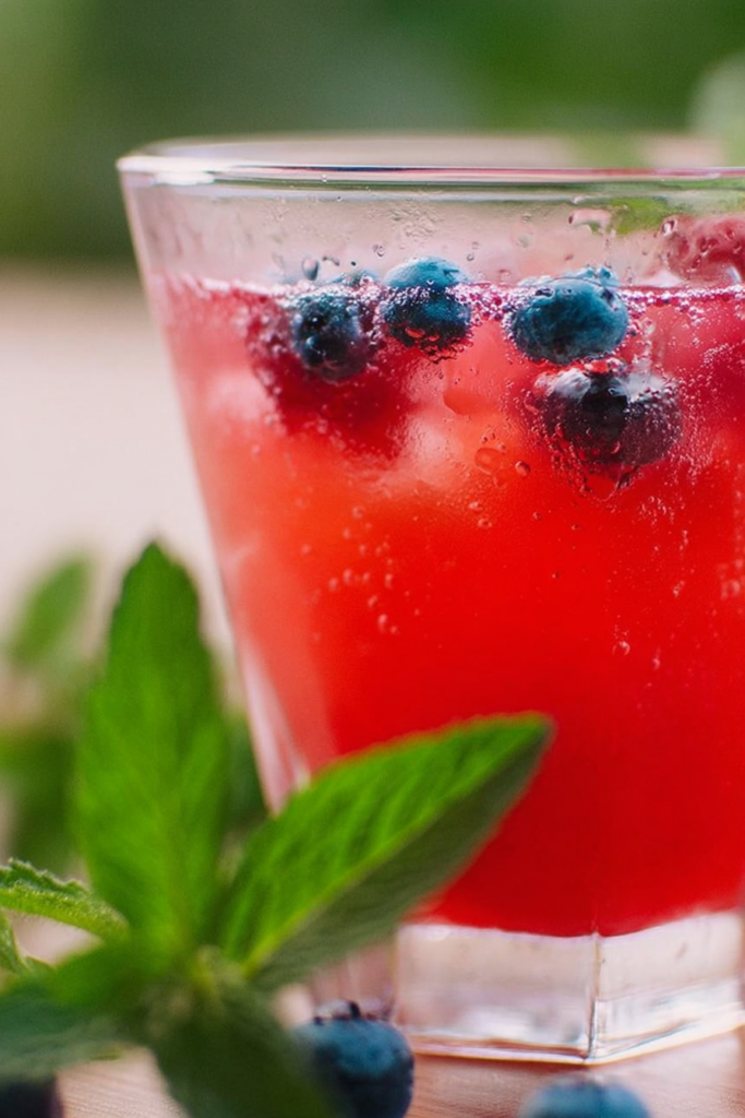 Refreshing blueberry raspberry iced tea cooler with fresh berries and lemon slices on a sunny table.