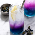 A refreshing glass of butterfly pea lemonade with ice, lemon slice and colorful blue to pink gradient.