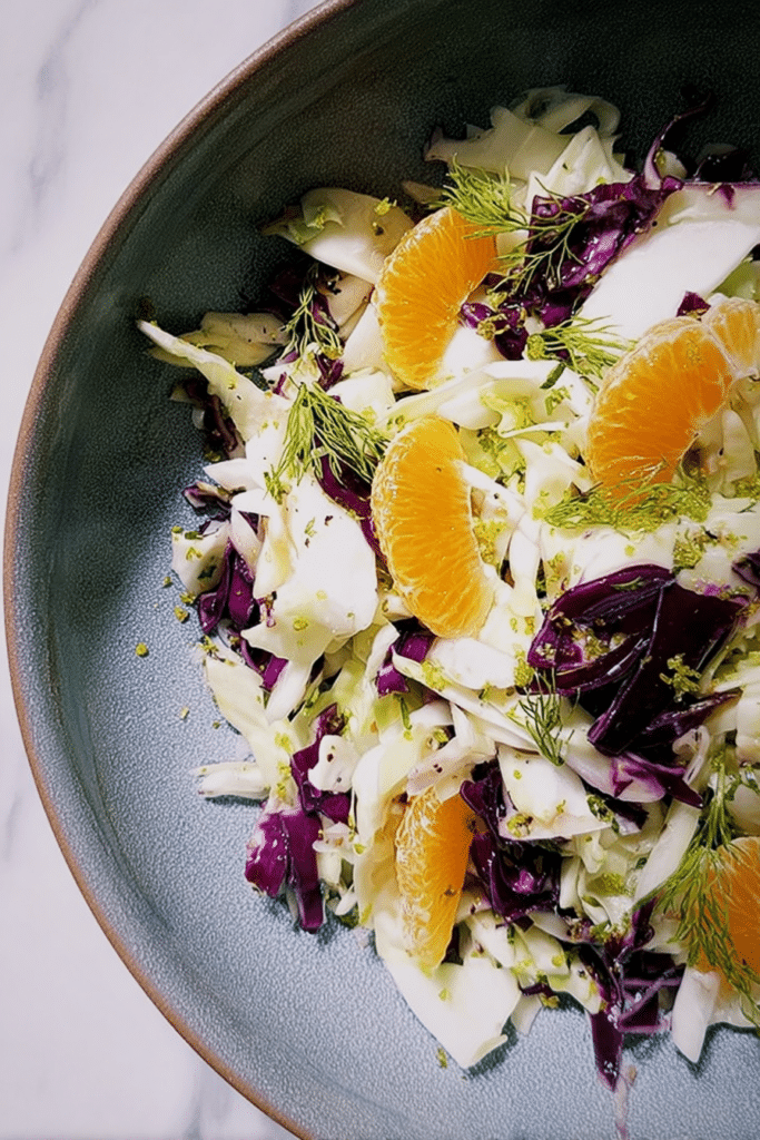 Vibrant cabbage, fennel, and citrus salad in a bowl featuring bright orange segments and green fennel fronds.