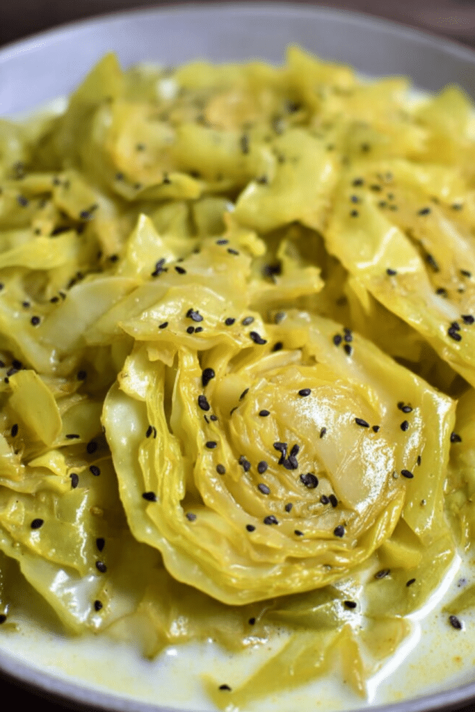 Bowl of cabbage in mild yogurt and mustard seed curry garnished with cilantro and served with rice.