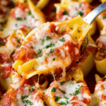 Cheesy stuffed shells filled with cheese and topped with marinara sauce and parsley, served on a plate.