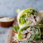 Close-up of a Chicken Caesar Wrap cut in half with lettuce, chicken, and parmesan cheese, served with Caesar dressing.