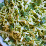 Fresh and colorful cilantro lime cabbage salad in a bowl with cilantro and lime garnishes.