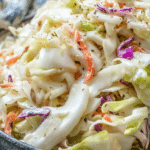Bowl of classic Memphis-style coleslaw with herbs and ingredients on a wooden table.