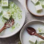 Coconut-and-lime jelly bowl garnished with lime zest and fresh coconut, on a colorful tropical background.