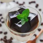 Delicious coffee jelly served in a bowl with a drizzle of cream and coffee beans on top.