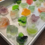 Colorful crystal gummies shaped like diamonds and cubes displayed on a decorative plate, highlighting their glossy texture and vibrant hues.