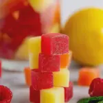 Colorful paleo homemade gummies made with real fruit on a flat lay with strawberries, oranges, and honey.