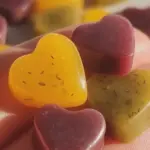 Colorful vegan gummies in various shapes made from fresh fruit purees, displayed on a wooden surface.