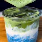 Earth Day matcha latte with layered blue spirulina and green matcha, decorated with yogurt clouds and spring flowers.