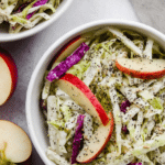 A fresh and colorful bowl of easy apple slaw with poppyseed dressing on a wooden table.