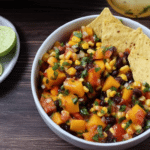 Bowl of easy peach salsa with chopped peaches, red bell pepper, and cilantro, next to crispy tortilla chips.