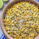 Delicious serving of esquites, a Mexican street corn salad, garnished with cilantro, lime, and cotija cheese, served in a bowl.