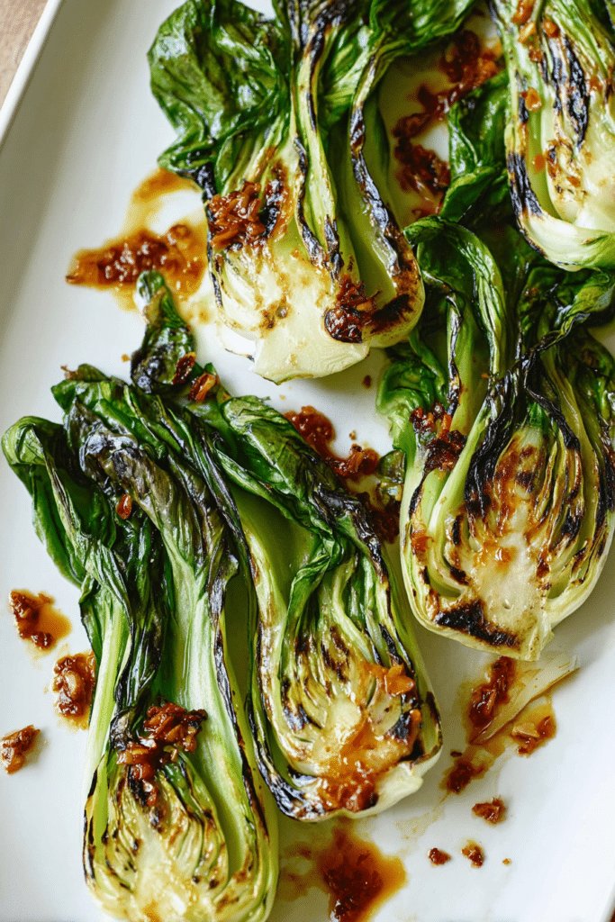 Grilled baby bok choy with ginger chili sauce served on a white plate, featuring a colorful presentation.