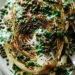 Close-up of grilled cabbage steaks with jalapeño chimichurri lentils and maple mustard tahini, garnished with parsley.