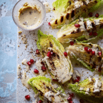 Grilled cabbage wedge topped with tahini dressing, pomegranate seeds, and toasted almonds on a wooden table.