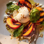 Grilled peach burrata salad with fresh basil and pine nuts on a wooden table.