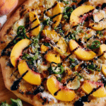 Close-up of grilled peach goat cheese pizza with jalapenos and fresh basil on a wooden cutting board.