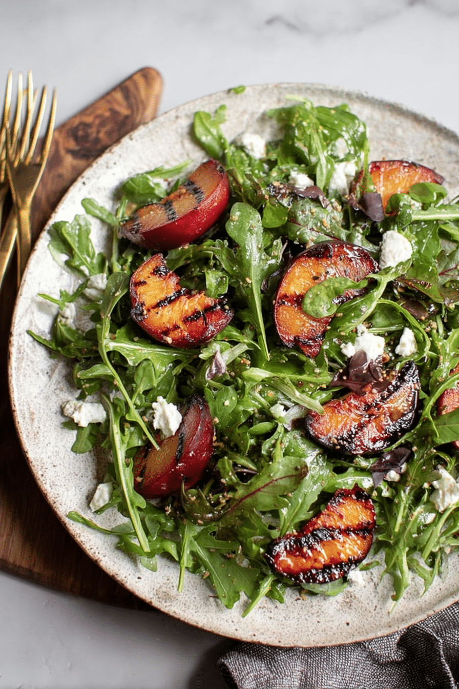 Grilled plum salad with goat cheese, arugula, and fresh herbs on a wooden table.