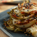 Grilled sesame ginger cabbage served on a wooden table with sesame seeds and soy sauce drizzle.